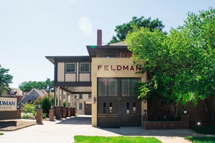 Two-story building with 'Feldman' sign and trees in front.