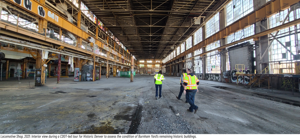 Empty industrial warehouse with three people in safety vests walking inside.