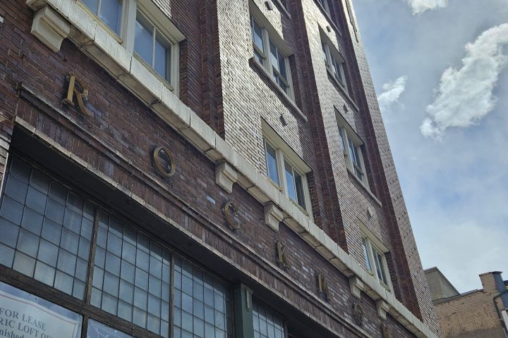 Tall brick building with large windows, viewed from below on a sunny day.