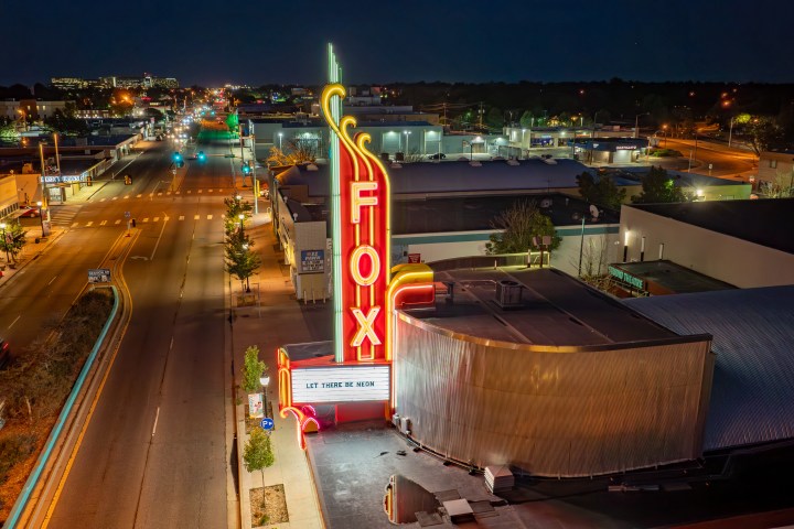 Night aerial view of the Fox Theater with bright neon lights on a city street.