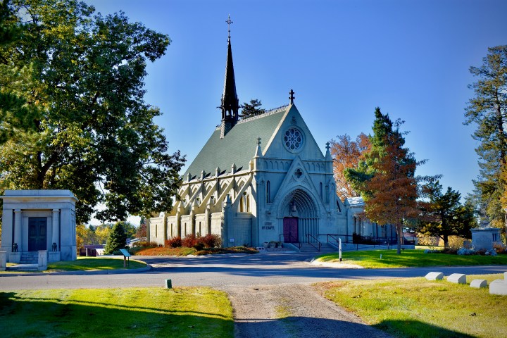A Gothic-style chapel with a tall spire, surrounded by trees under a clear blue sky.