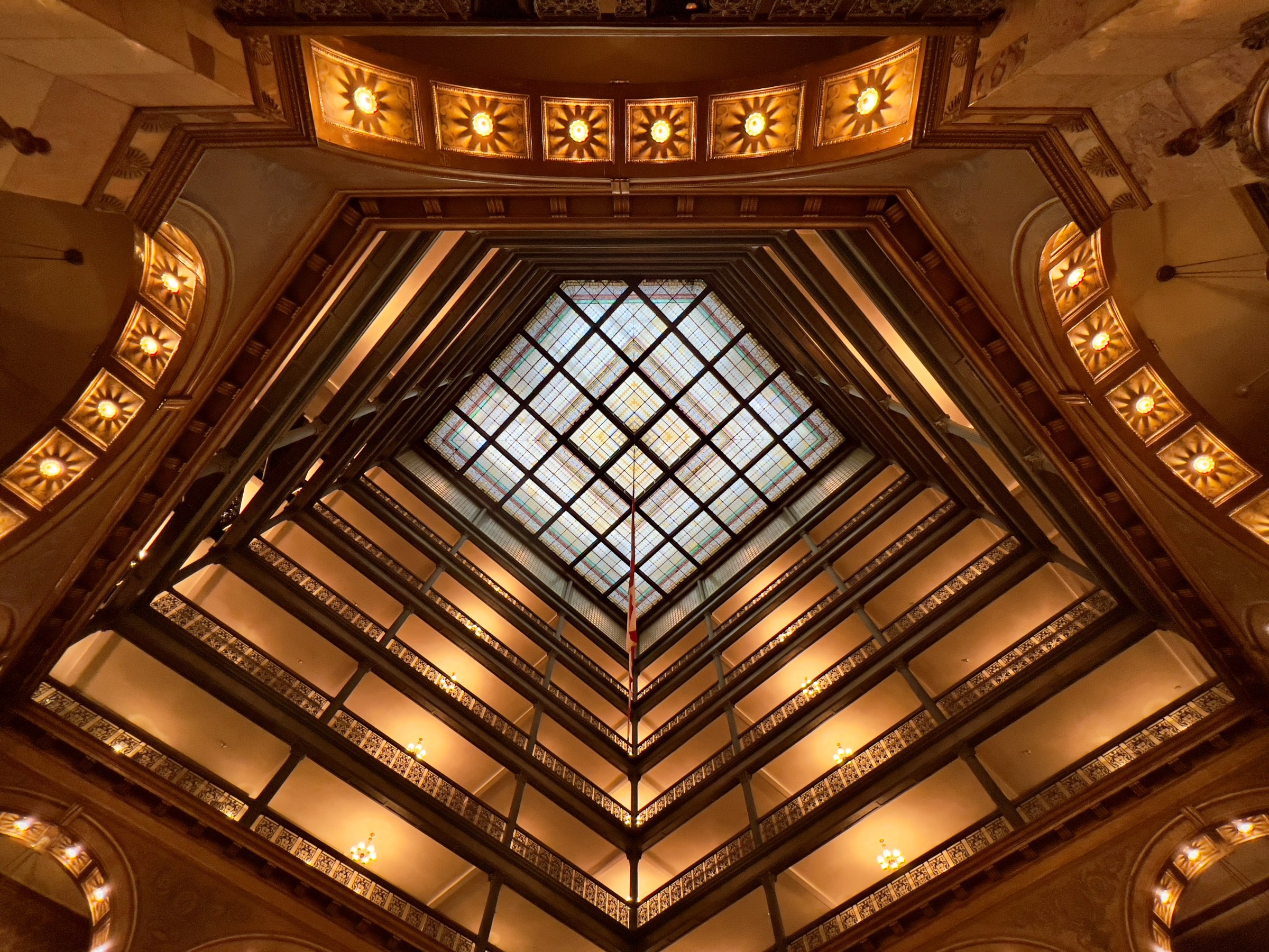 View up a grand atrium with ornate balconies and a stained-glass ceiling.