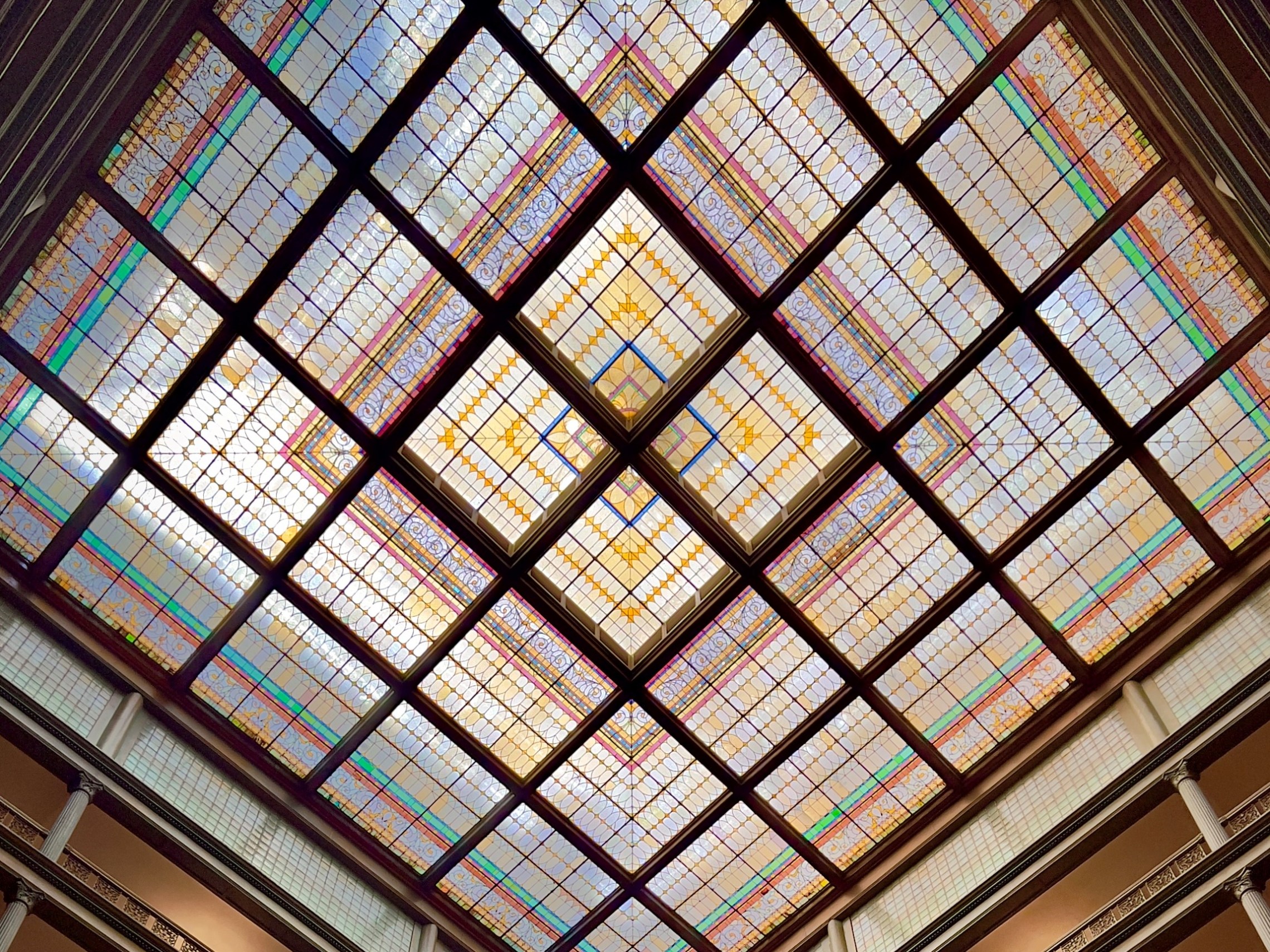 Colorful stained glass ceiling with geometric patterns in an ornate building.
