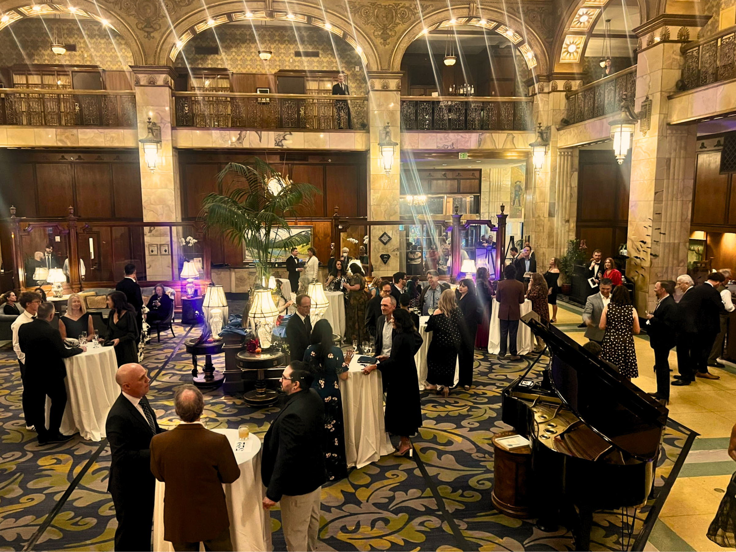 Elegant gathering in a grand hall with arches, people mingling around cocktail tables.