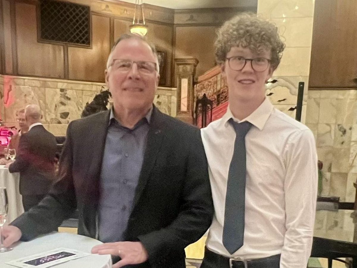 Two men in formal attire standing by a table with a white tablecloth at an indoor event.