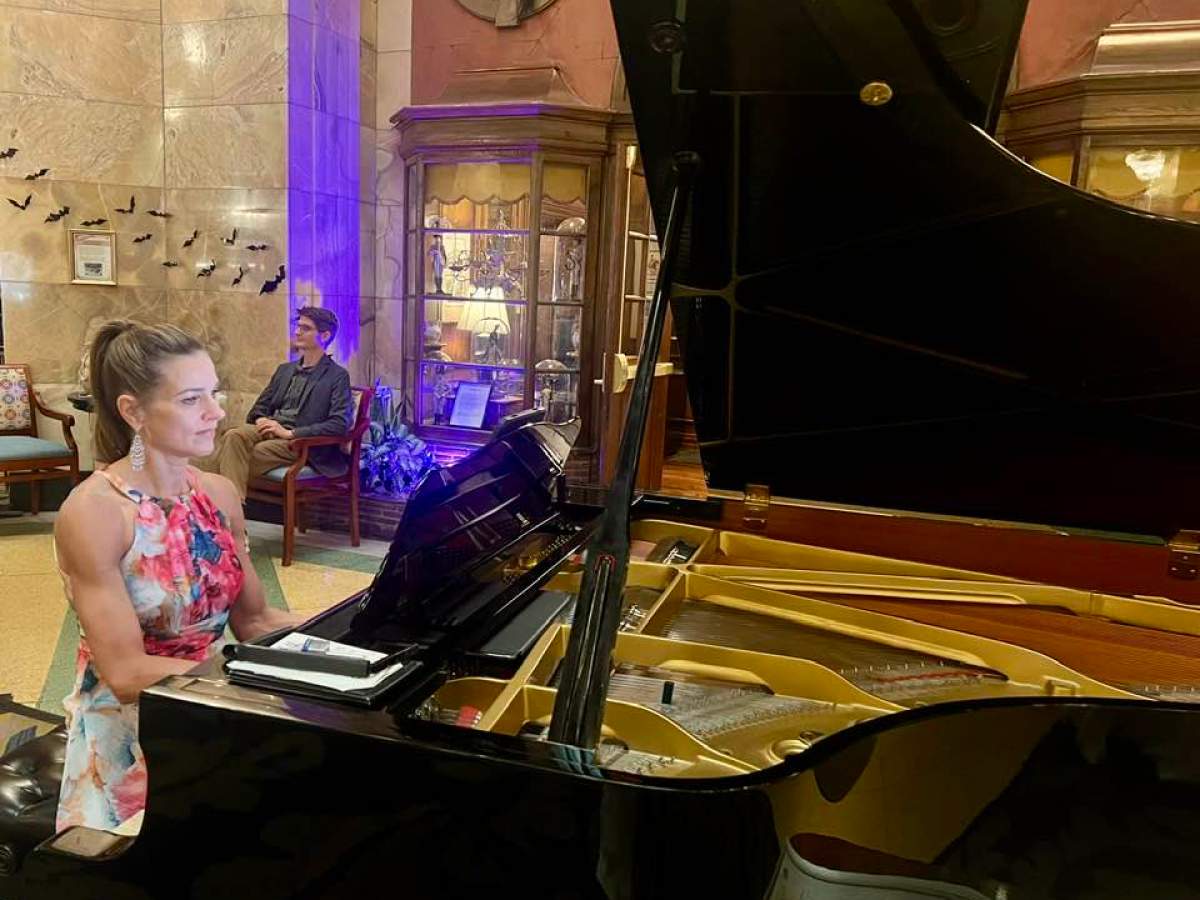 Woman in floral dress playing a grand piano in an elegant room.