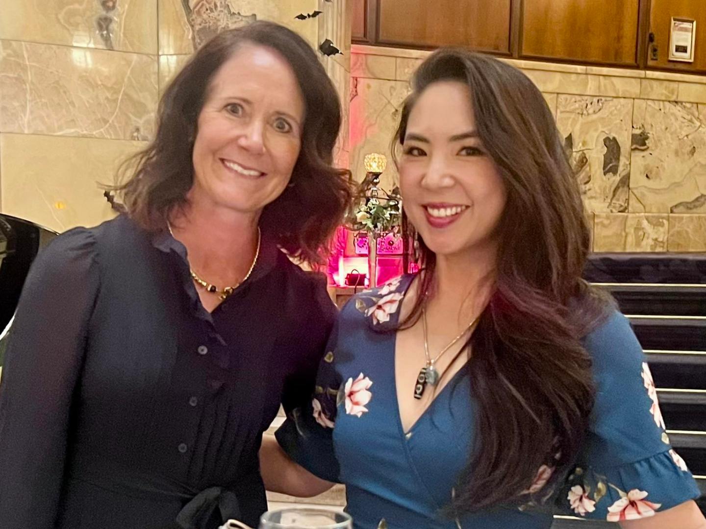 Two women smiling at a table with wine glass and purse in elegant setting.
