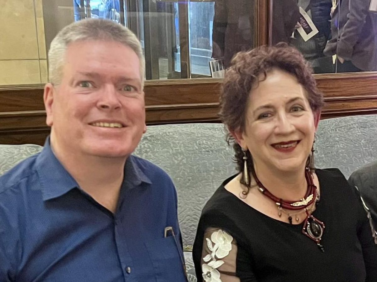 A smiling man and woman sitting together indoors with a glass of champagne on the table.