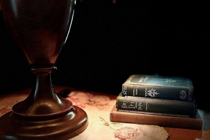 Vintage lamp on table with lace cloth and stacked books in warm light.