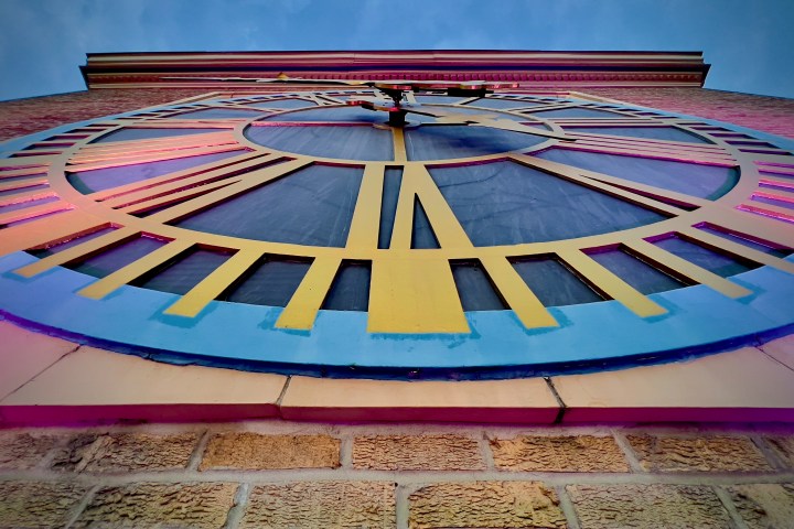 Upward view of a colorful outdoor clock on a brick wall.
