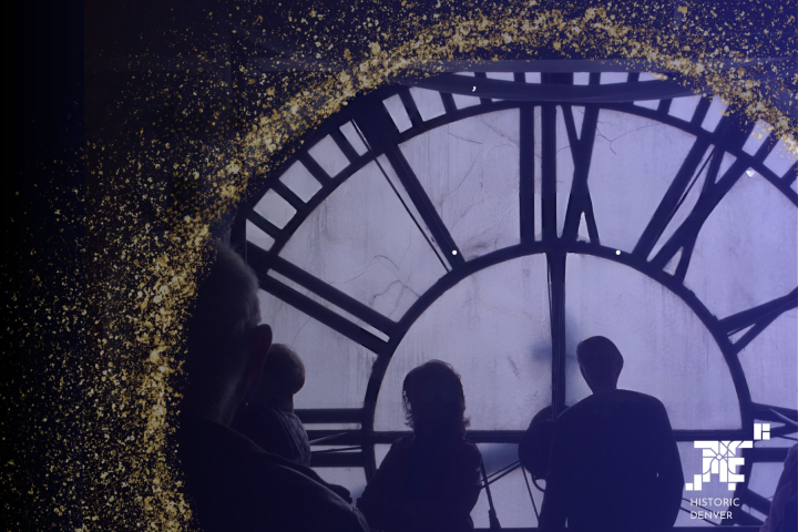 Silhouettes of people in front of a large clock face with gold speckles on the edges.