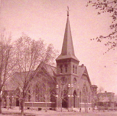 Sepia-toned image of a church with a tall steeple and bare trees in the foreground.