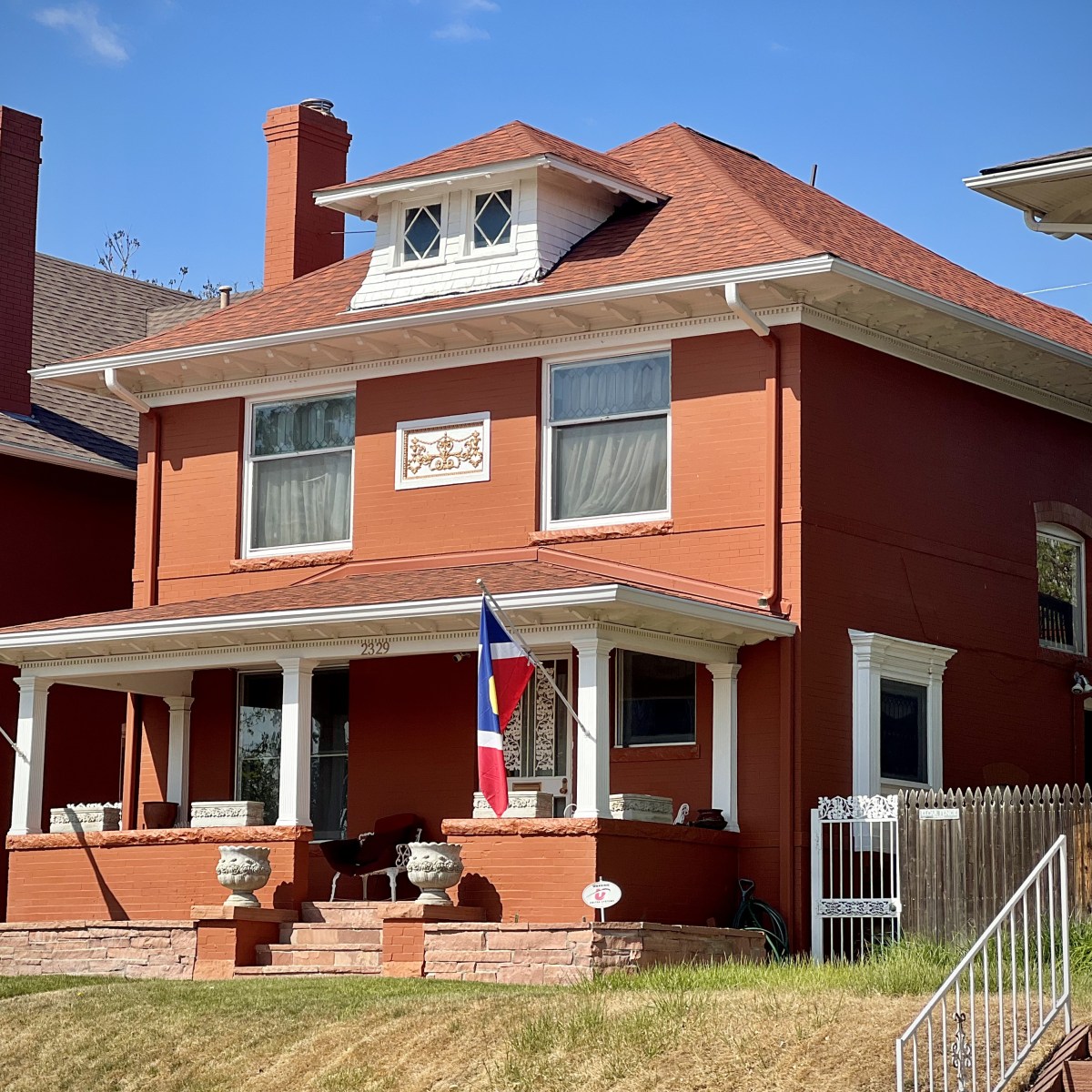 Red brick house with flags on porch and small front yard.